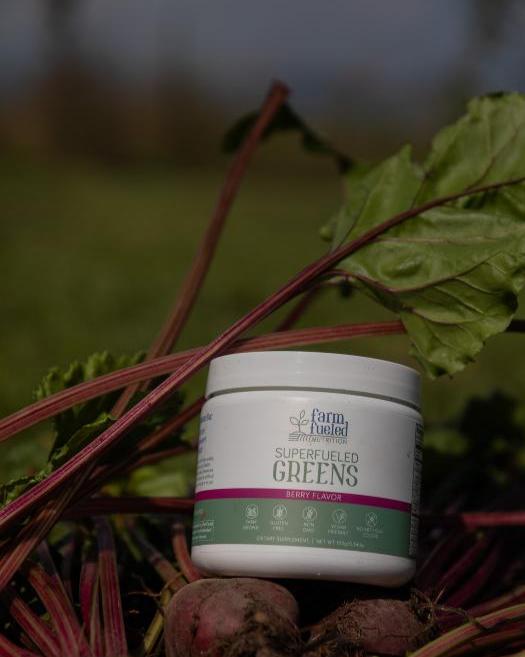 A canister of Superfueled greens powder sits on fresh picked beets with the greens surrounding it.