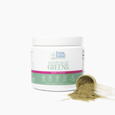 The white and green Superfueled Greens canister (Berry Flavor highlighted in pink) displayed in front of a white background, next to a clear plastic scoop overflowing with delicious greens powder in the bottom right corner.