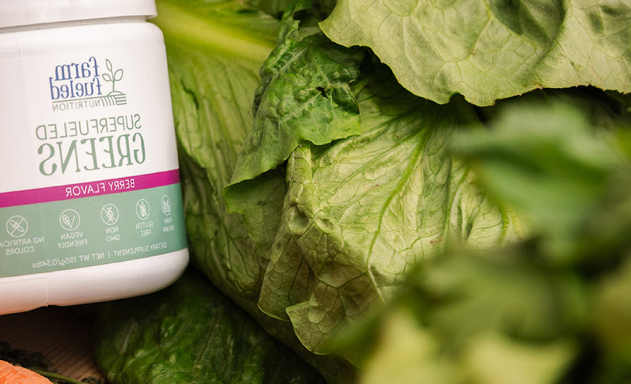 A Superfueled Greens canister peeks into the corner of the image, laying on a bed of large, fresh vegetable greens.